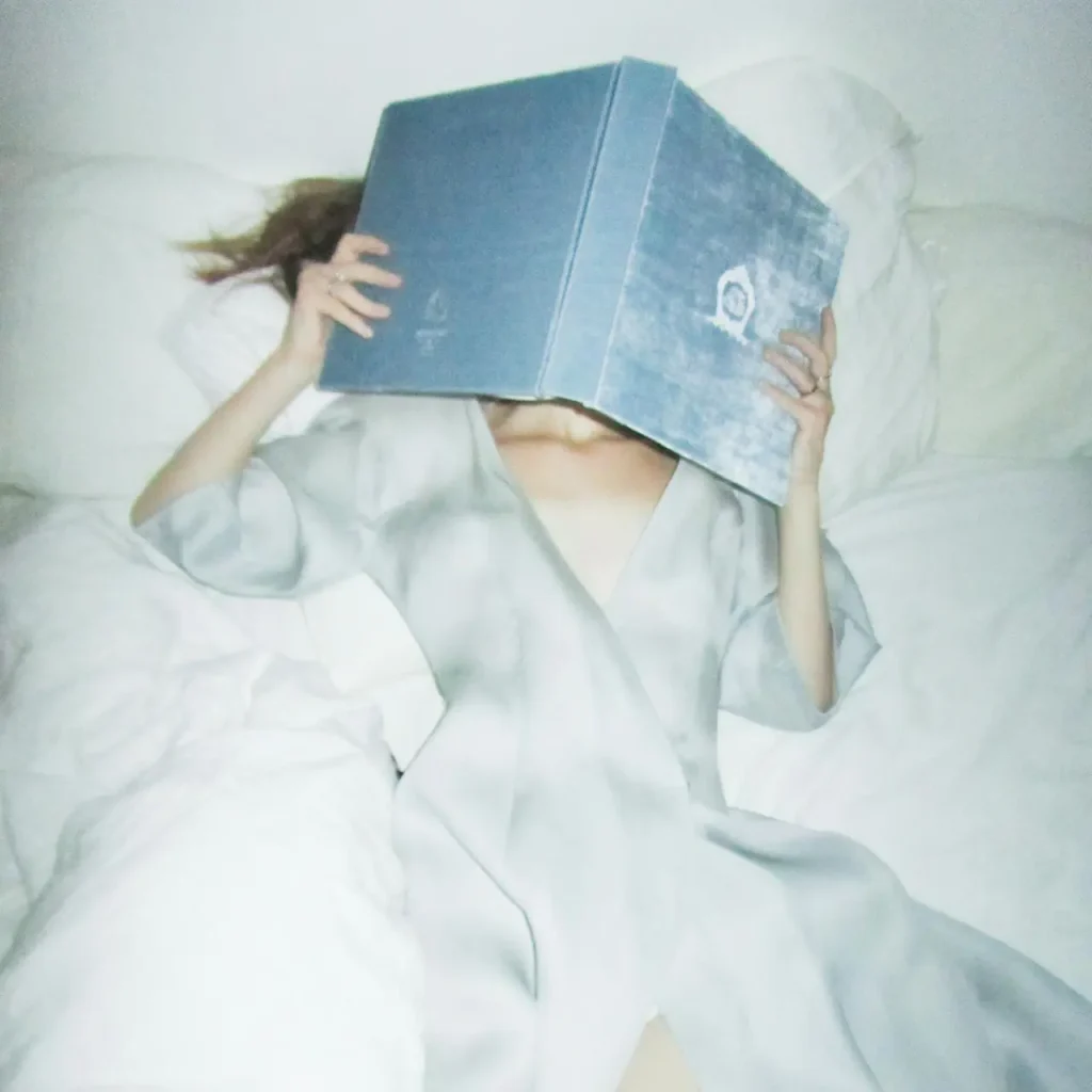 Kobieta spokojnie czyta książkę, praktykując czytanie mindfulness w zaciszu domowym, z filiżanką herbaty obok.